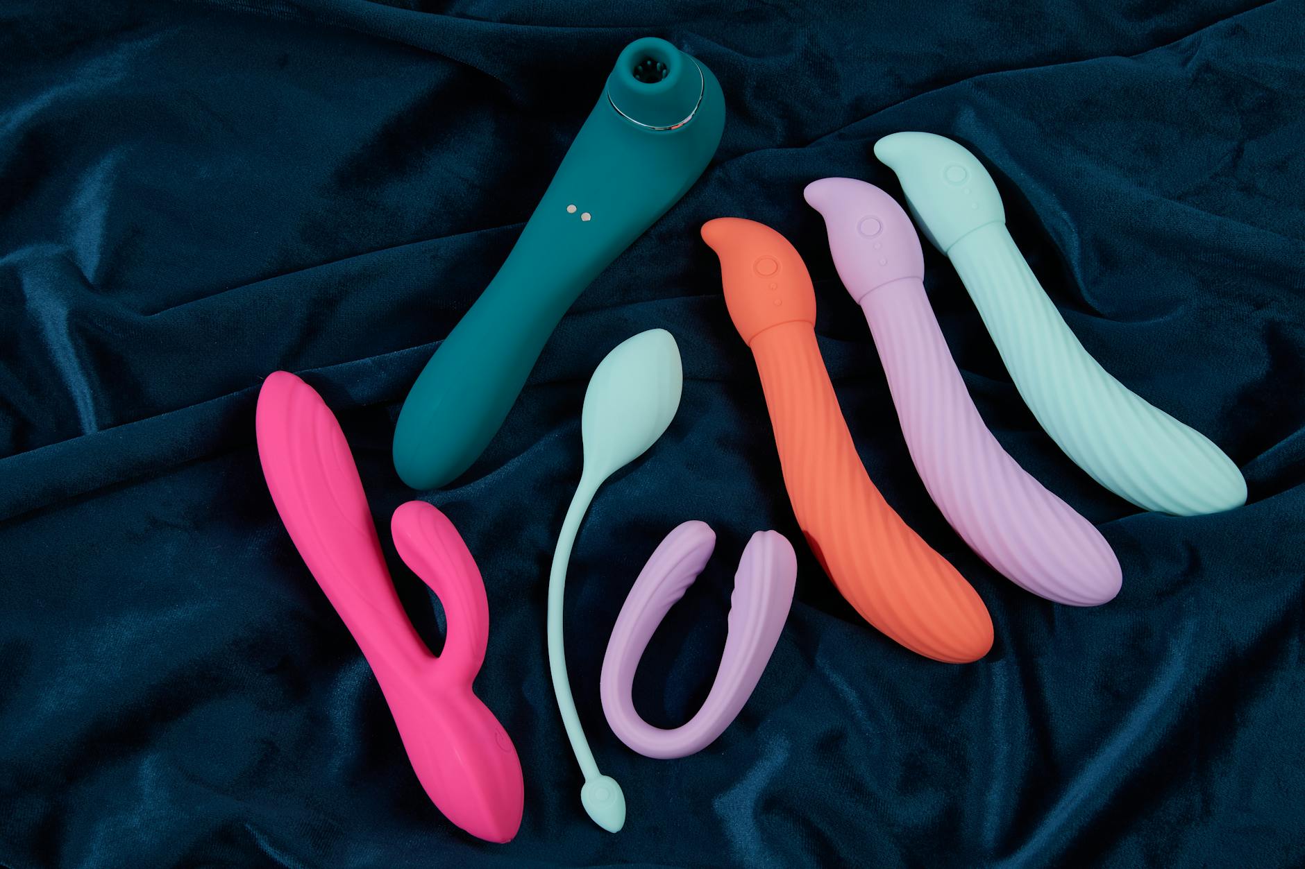 Colorful silicone sex toys displayed on dark fabric, showing texture and shape variety