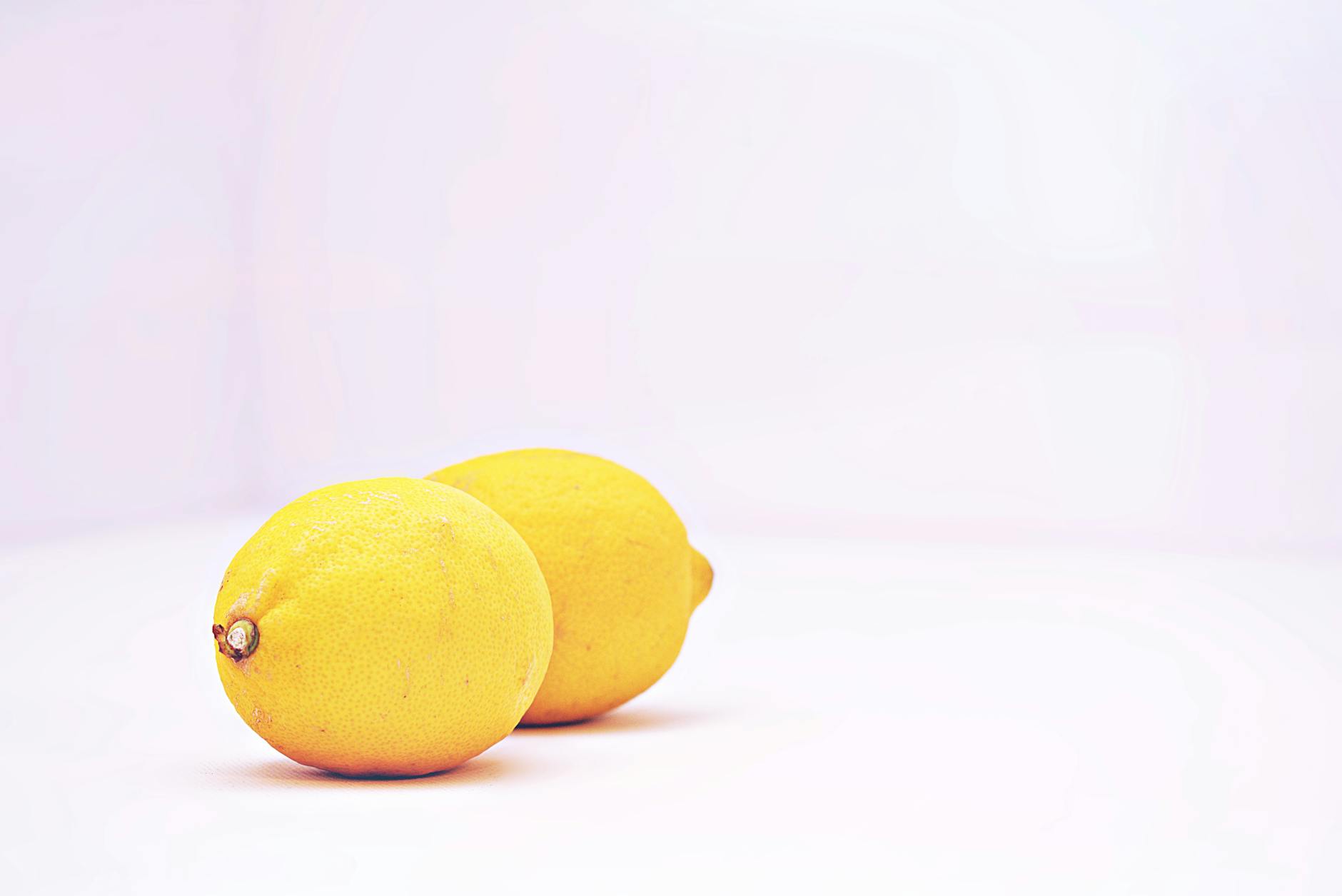 A hand holding a lemon on a soft pink background, symbolizing natural pleasure and intimate connection.