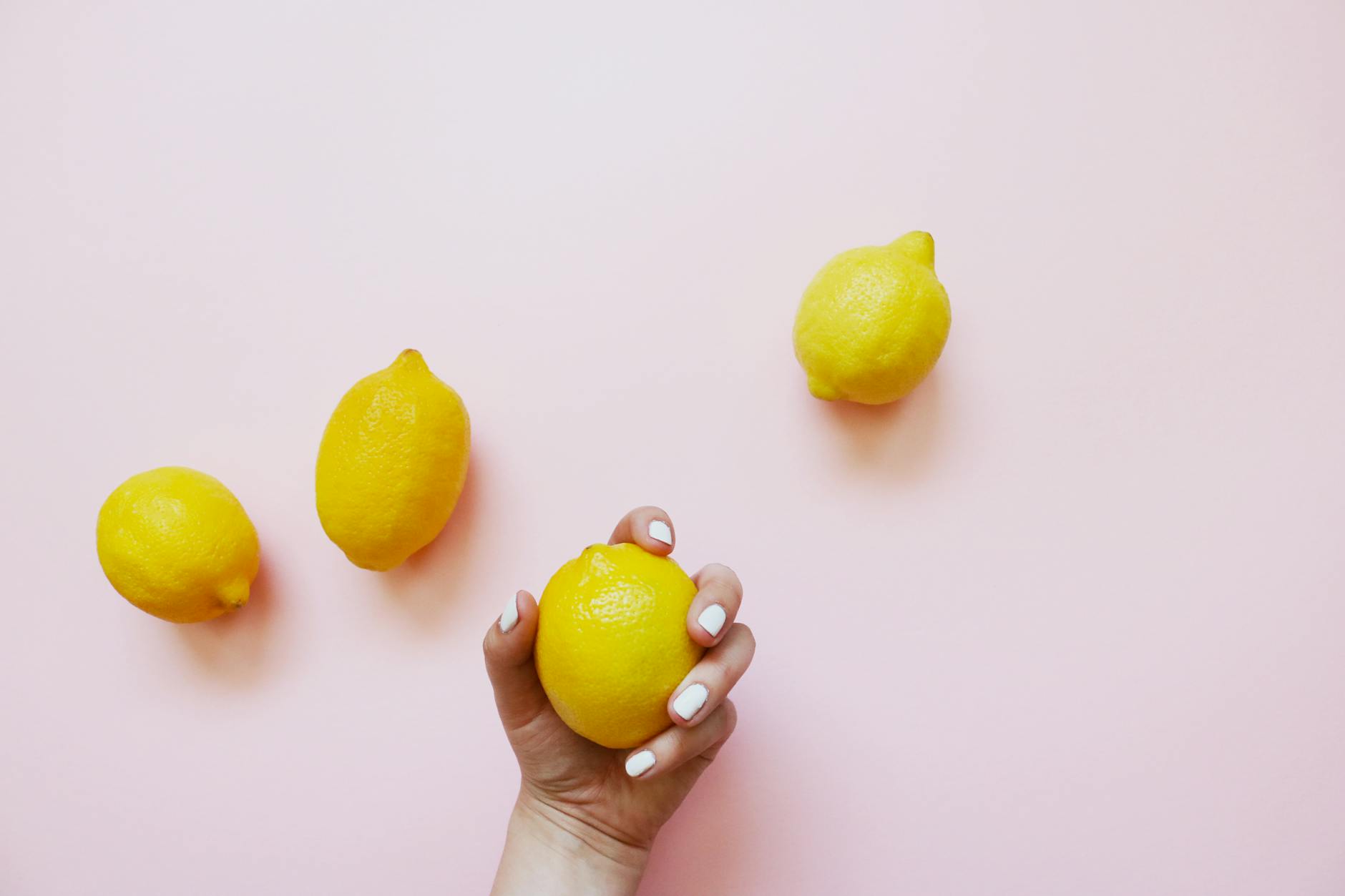 A hand holding a lemon against a soft pink background, representing fresh clitoral sensation