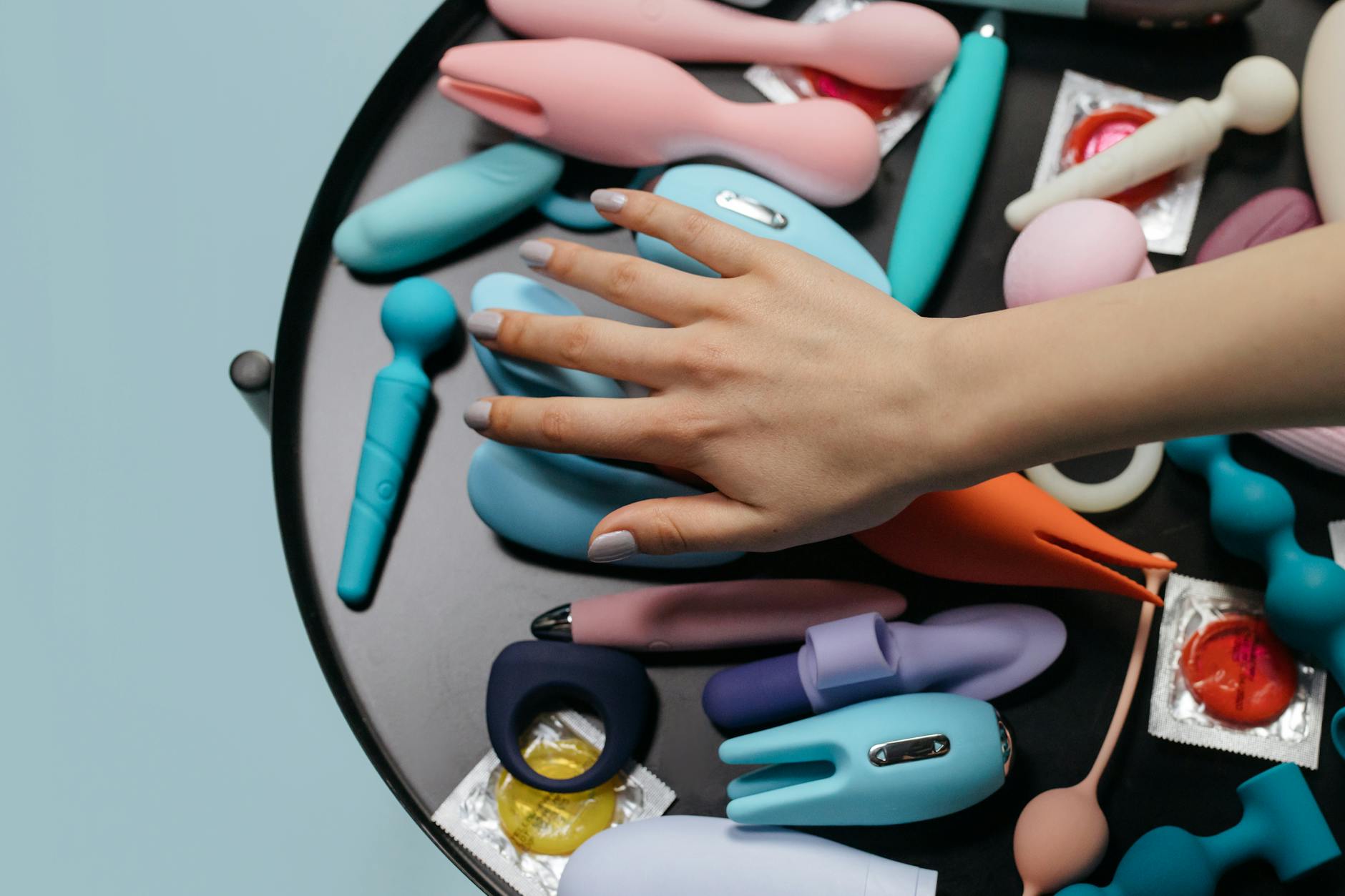 A hand reaching over a variety of colorful lemon clitoral vibrators arranged on a soft surface.