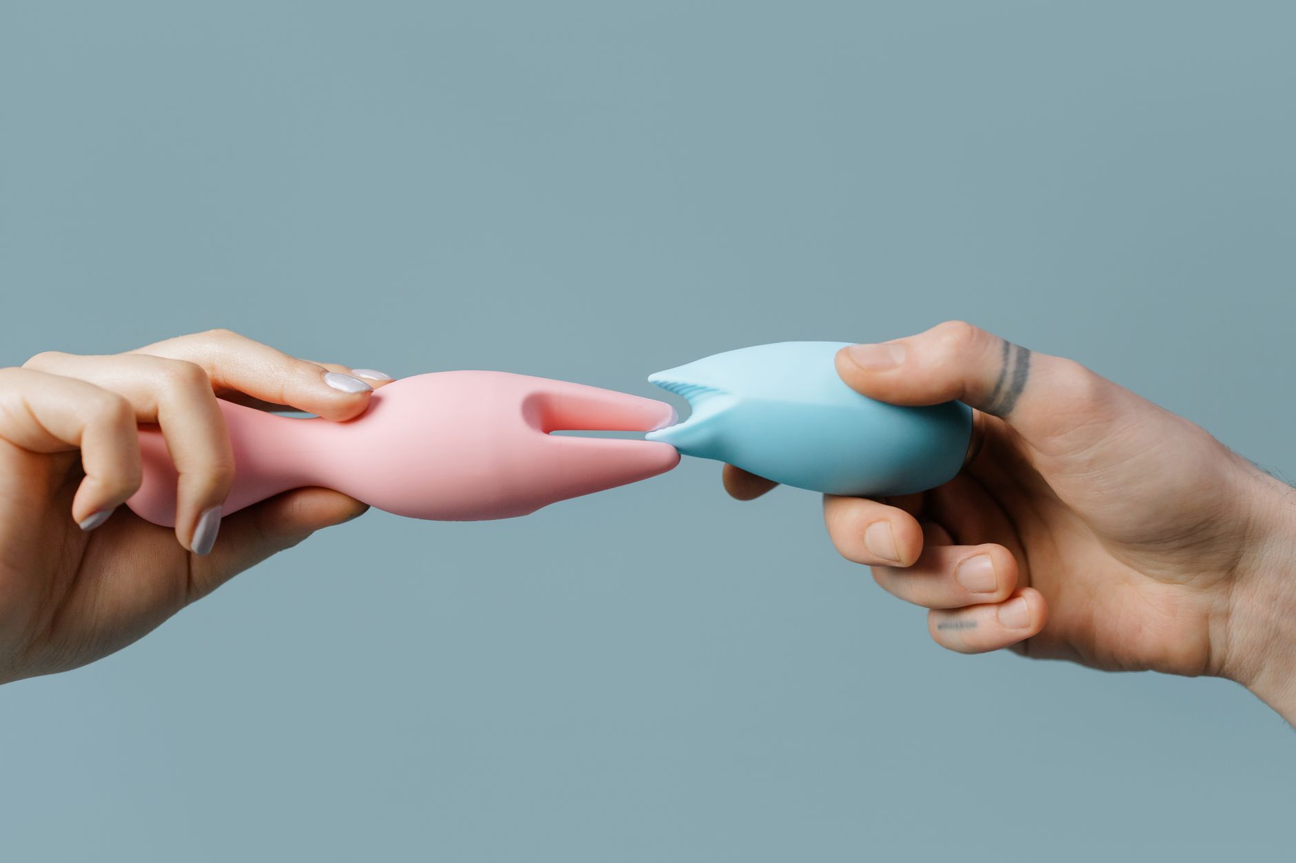 Hands holding colorful silicone vibrators against a soft pastel background