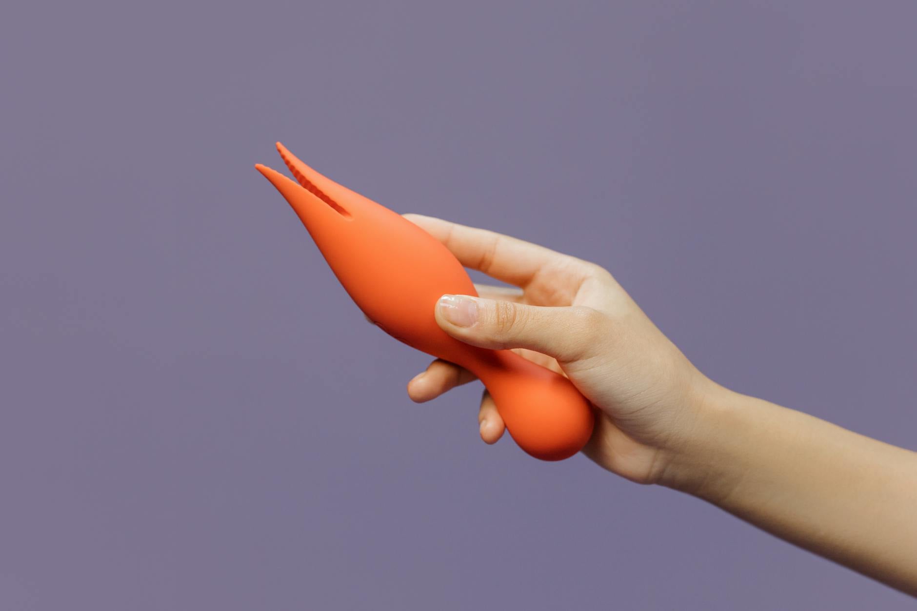 A hand holding a vibrant lemon clitoral vibrator against a minimalistic purple backdrop