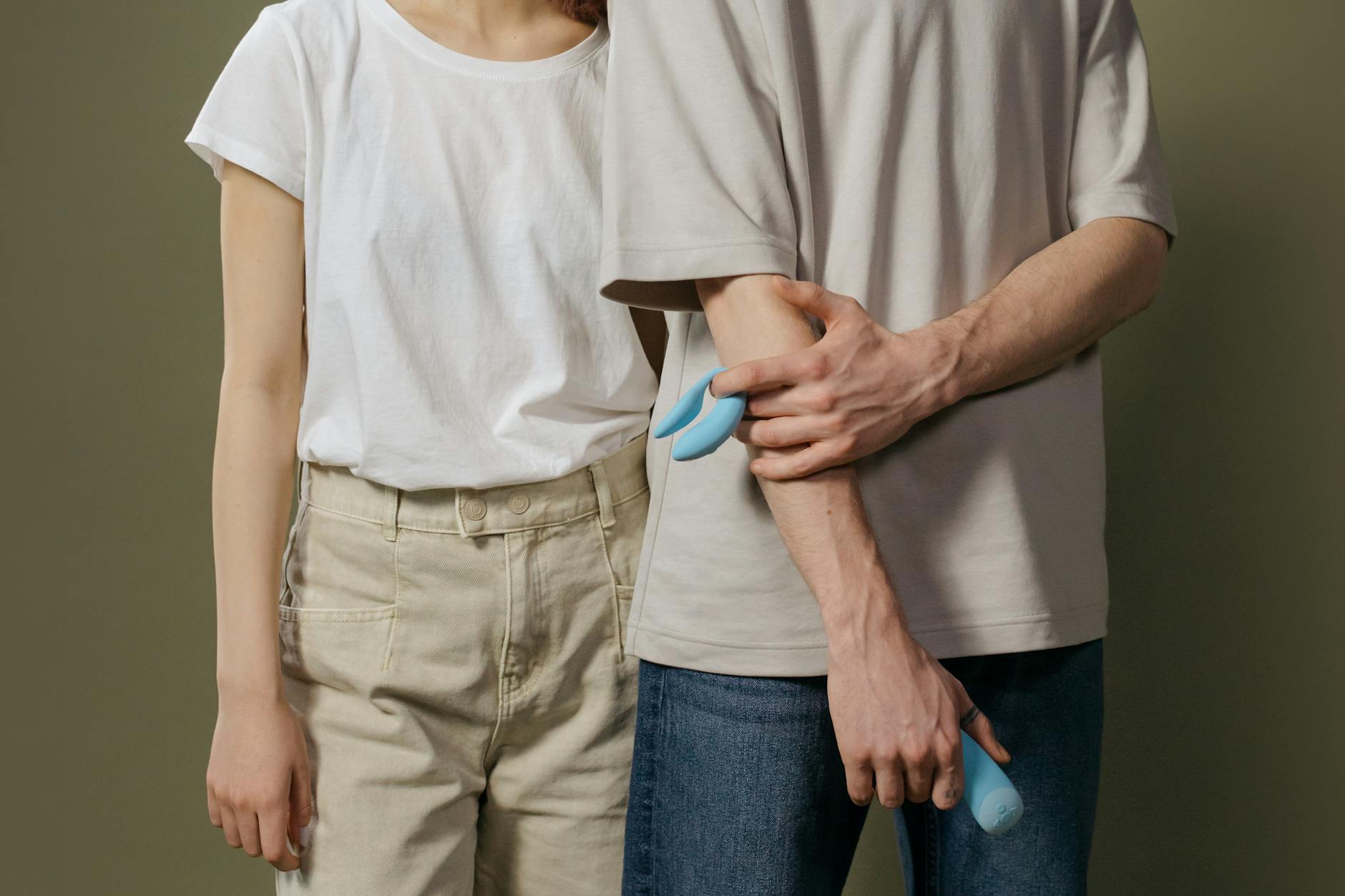 A young couple standing together indoors, holding a blue vibrator, symbolizing modern intimacy and trust.