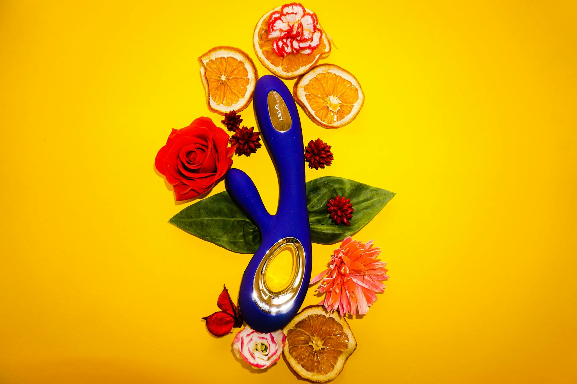 A blue lemon vibrator surrounded by fresh lemons and flowers on a yellow background